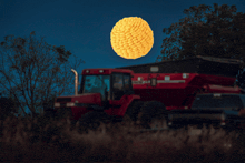 a tractor is parked in a field at night with a full moon behind it