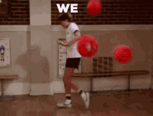 a boy is playing with red balls in a gym and the word we is on the wall behind him .