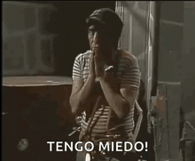 a man in a striped shirt is standing in a dark room with his hands folded and says tengo miedo !