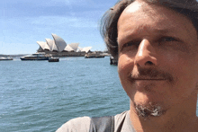 a man stands in front of a body of water with the sydney opera house in the background