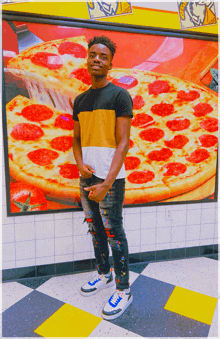 a man stands in front of a large pepperoni pizza advertisement