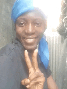 a man wearing a blue head scarf is smiling and giving a peace sign