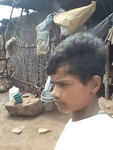 a young boy stands in front of a shed with a bucket and a water container