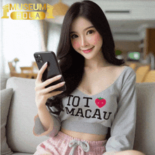 a woman wearing a shirt that says " i love macau " holds a cell phone