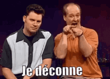 two men are sitting next to each other and one of them is pointing at the other with the words je deconne written on it .