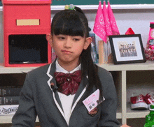 a girl in a school uniform is sitting in front of a shelf with a picture of a group of people in a frame .