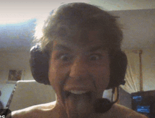 a shirtless man wearing headphones and a microphone is sticking his tongue out