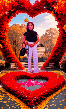 a woman is standing in front of a heart made of red flowers .