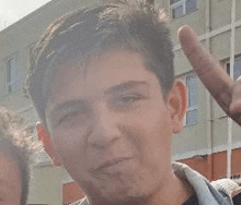 a young man is making a funny face and giving a peace sign .