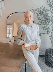 a woman wearing a hijab holds a bowl of food