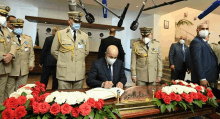 a man wearing a mask is signing a book with flowers in front of him