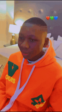 a young man wearing an orange hoodie is sitting on a bed in a bedroom .