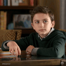 a young boy sits at a table with his hand on a piece of paper that says manifest on it