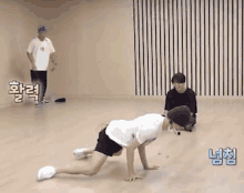 a man is doing a handstand on a wooden floor while two other men look on .