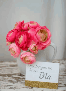 a bouquet of pink flowers in a vase with a card that says que tengas un buen dia