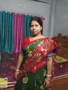 a woman in a red and green saree stands in front of a bed with a mattress on it