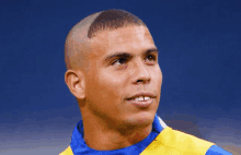 a man with a shaved head wearing a yellow and blue shirt