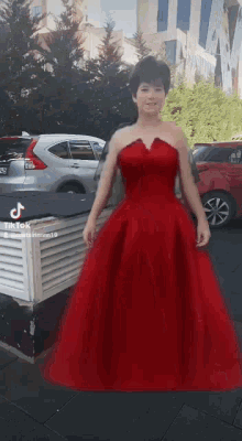 a woman in a red dress is standing in front of a car parked in a parking lot .