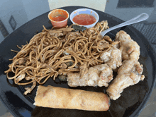 a black plate topped with noodles and fried chicken