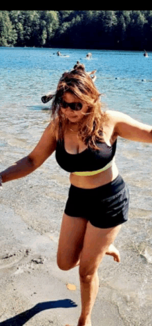 a woman in a bikini and shorts is standing on a beach near a lake .