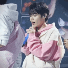 a boy in a pink hoodie is singing into a microphone