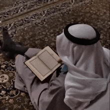 a man in a white robe is reading a book while sitting on the floor .