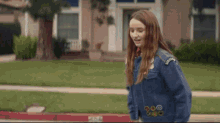 a woman in a blue jacket is walking down a sidewalk in front of a house with the words welcome in the background