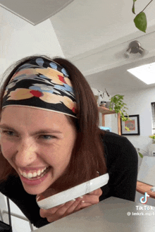 a woman wearing a headband is smiling and holding a white item with a tiktok watermark