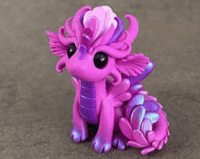 a purple and purple clay dragon figurine is sitting on a gray surface .