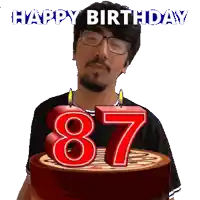 a man with glasses is holding a birthday cake with candles that say 87