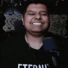 a man wearing a black shirt with the word eternit on it is standing in front of a microphone and smiling .