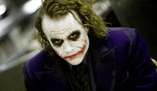 the joker is wearing a purple suit and tie and is looking at the camera