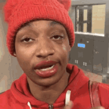 a woman wearing a red beanie and a red hoodie makes a face