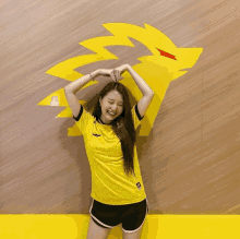 a woman wearing a yellow shirt and black shorts stands in front of a yellow lion on a wall