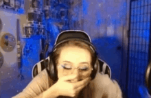 a woman wearing headphones and glasses is covering her mouth with her hand while sitting in a gaming chair .