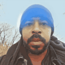 a man with a beard wearing a blue beanie and a black jacket