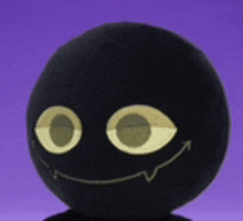 a black stuffed animal with a smiley face on it is sitting on a table .