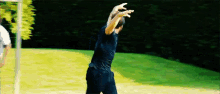 a man in a black shirt is standing on a lush green field with his arms outstretched .