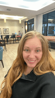 a woman with long blonde hair is smiling in a room with tables and chairs