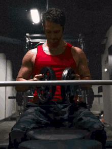 a man in a red tank top holds a barbell