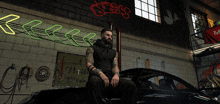 a man sits on the hood of a car in a garage under a neon sign that says ' oasis '