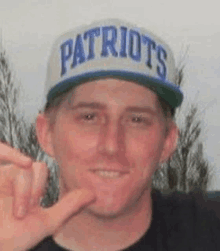 a man wearing a patriots hat is making a peace sign with his hand .