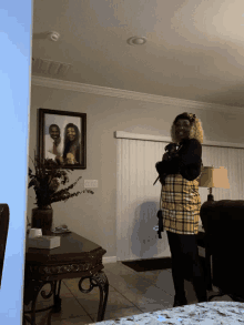 a woman in a plaid skirt stands in a living room in front of a picture of a family