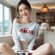 a woman sits on a couch wearing a toto macau sweatshirt