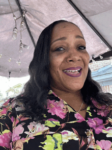 a woman wearing a floral shirt and purple lipstick smiles for the camera