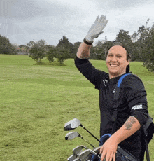 a man holding a bag of golf clubs is wearing a black shirt that says ' ping ' on the sleeve