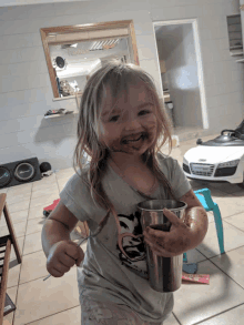 a little girl with her face covered in chocolate holding a cup and spoon