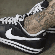 a person with a tattoo on their leg wearing a pair of black and white nike sneakers .