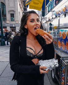 a woman in a bra is eating a sandwich in front of a yellow sign that says ' subway '