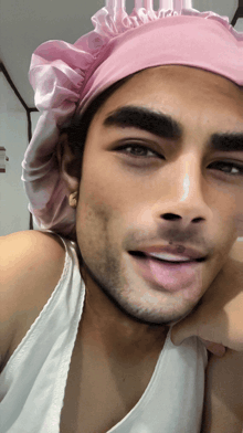 a man wearing a pink hat and a white tank top looks at the camera